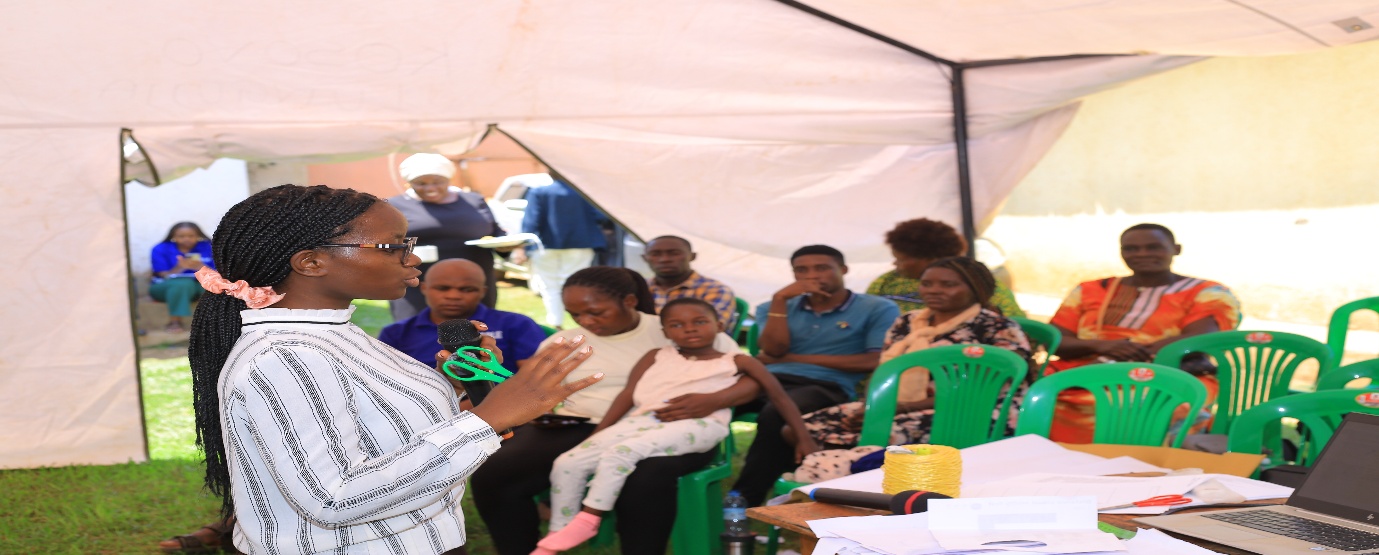 A community volunteer speaks to a group seated under a tent at an eye outreach