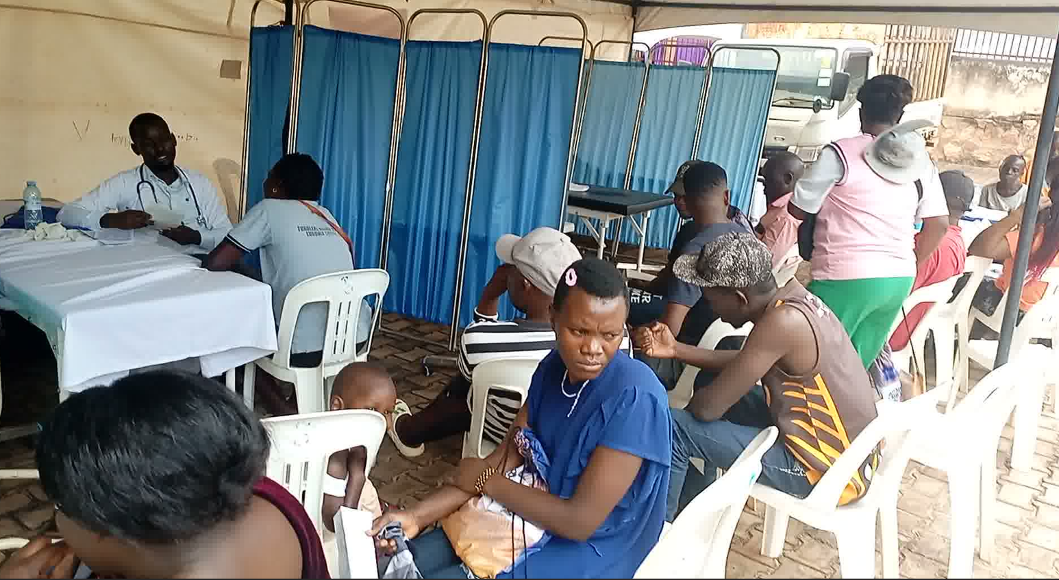 Community members queue under a tent at an integrated community outreach