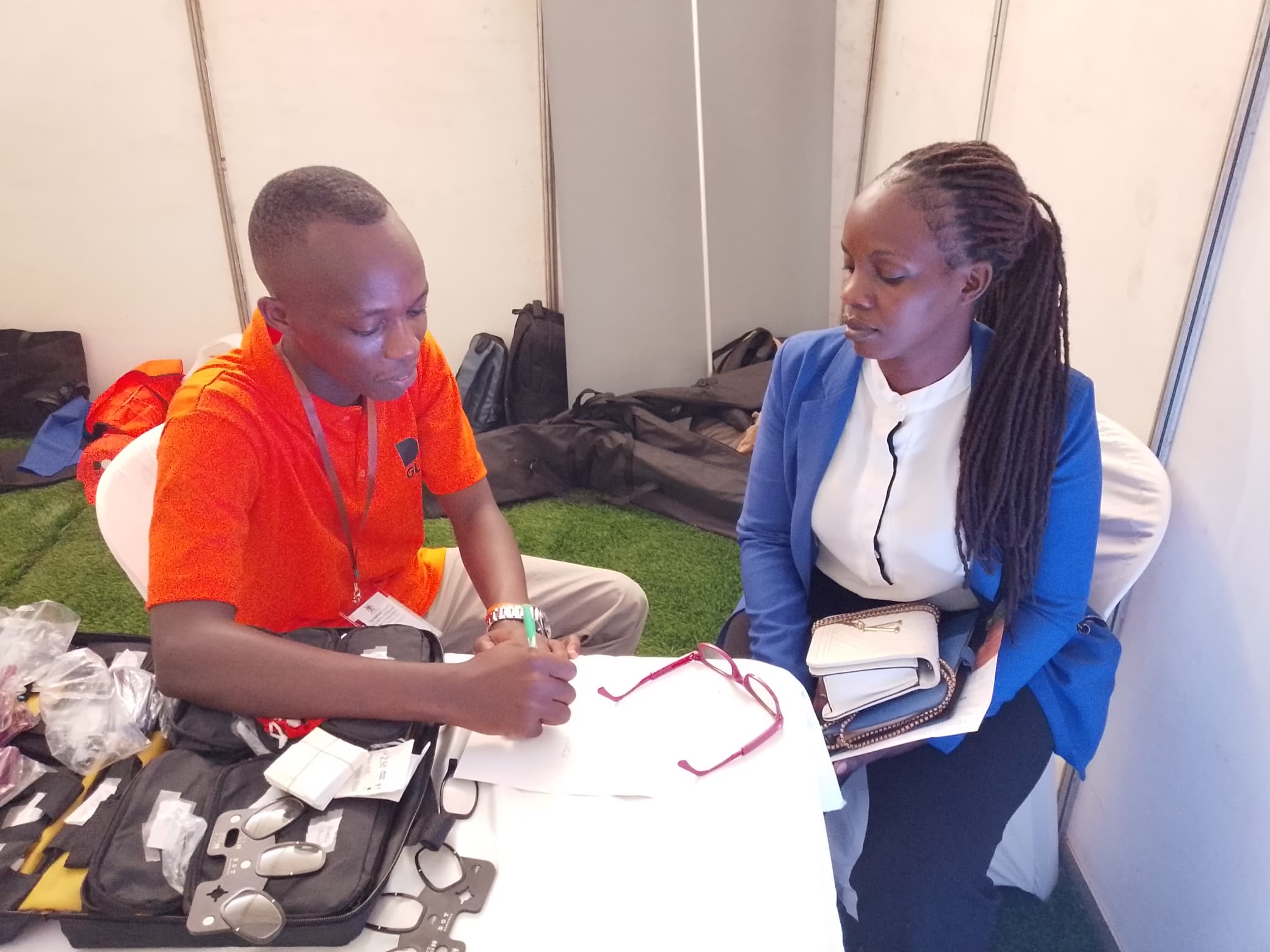 A health worker fits reading glasses for a woman at a screening desk