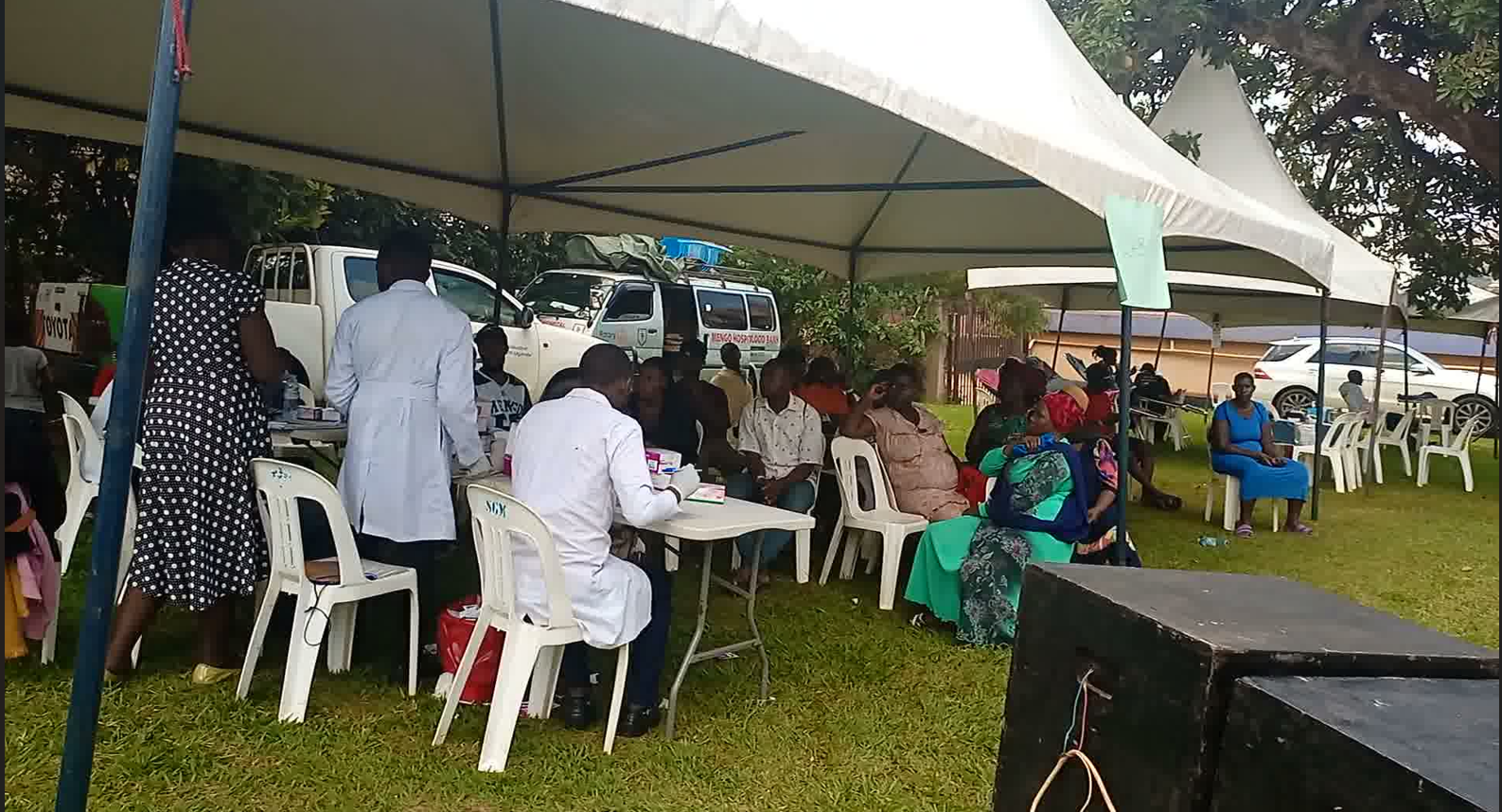 Health workers at tables under a white tent screening community members on a grassy field