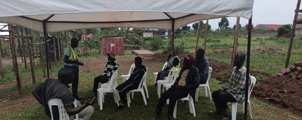 Community members sit under a canopy during a village dialogue in Kakiri