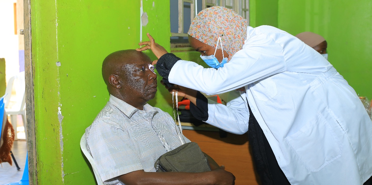 A health worker checks the eyes of a man in a green-walled room during a community eye outreach